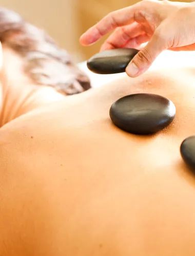 Woman receiving a relaxing hot stone massage with smooth black stones placed on their back.