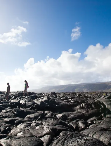 Visitors walking along a rocky coastal path under a clear blue sky.