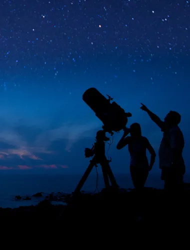 Astronomers using telescopes under a star-filled sky.