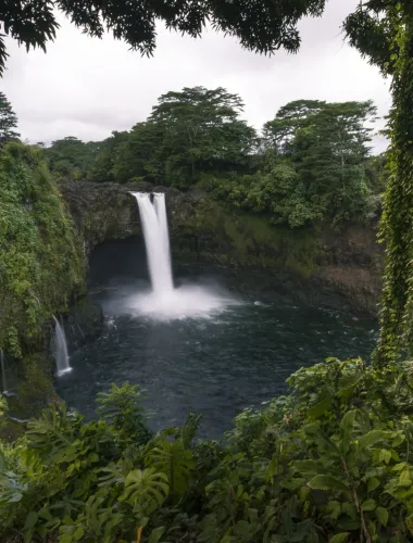 Rainbow Falls cascading into a pool surrounded by dense tropical vegetation.