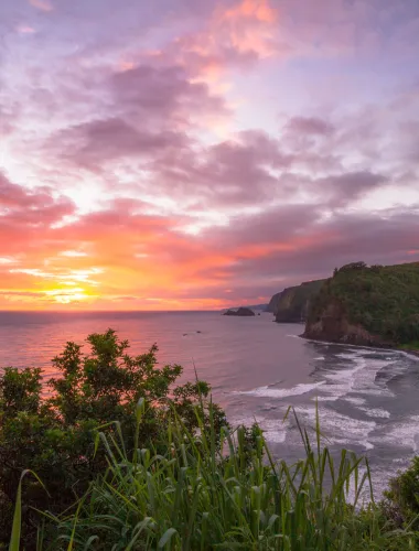 Scenic view from Pololu Valley Lookout at sunset, overlooking a lush valley, black sand beach, and the northeastern coastline.