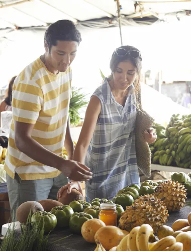 Couple browsing fresh fruits and vegetables at an outdoor farmers market in Hilo.