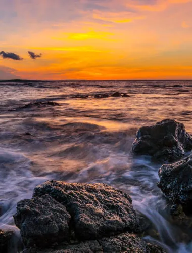 Ocean sunset with waves crashing against rocks in the foreground