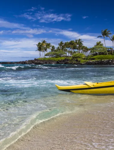 Yellow kayak on a crystal-clear beach with lush greenery in the background.