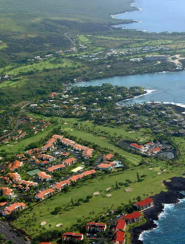 Aerial view of the Keauhou resort area, featuring lush green golf courses, homes, and the Pacific Ocean.