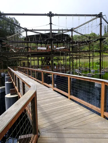 Exterior image of a wooden bridge leading to a ropes course. 