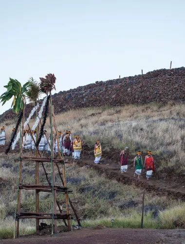 Visitors walking toward Puukohola Heiau, a historic temple surrounded by dry grassland under a clear blue sky.