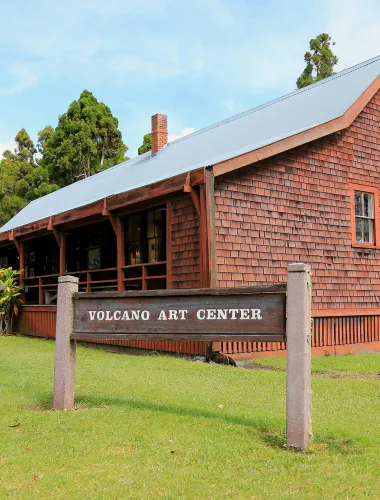 The Volcano Art Center, a rustic wooden building with a grassy lawn, located in Volcano Village.