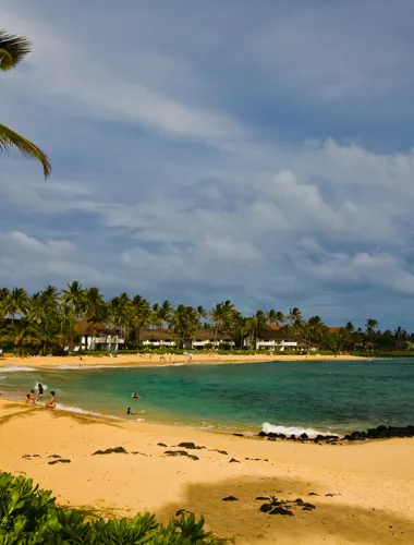 Poipu Beach Park with golden sand and clear water surrounded by lush greenery.