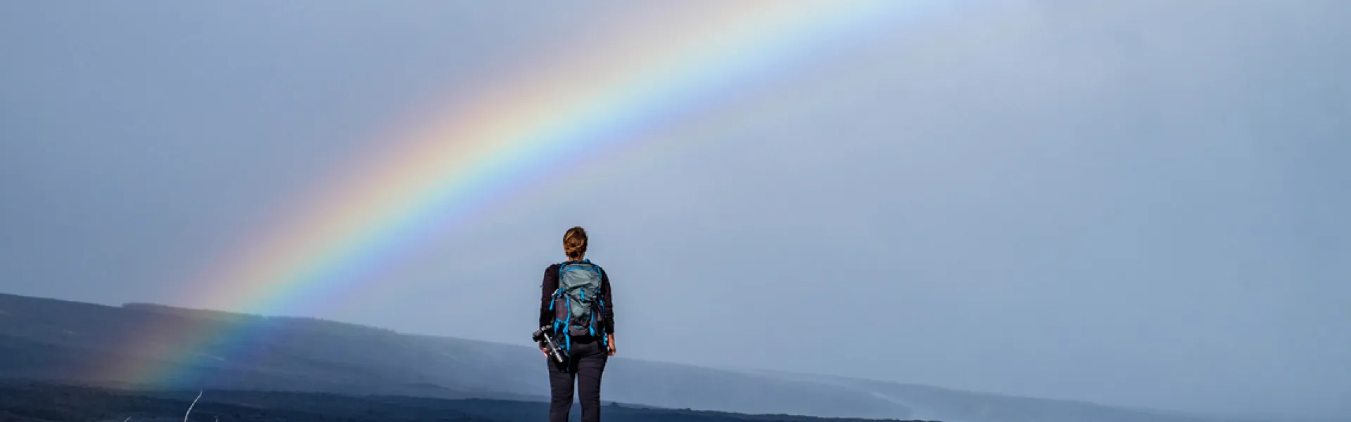 Hiker with a backpack looking at a rainbow 