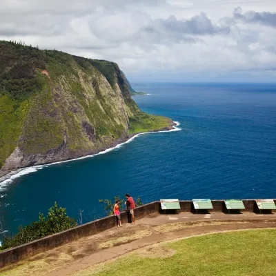 Couple enjoying a scenic view of steep green cliffs and the deep blue ocean at Waipio Valley Lookout.