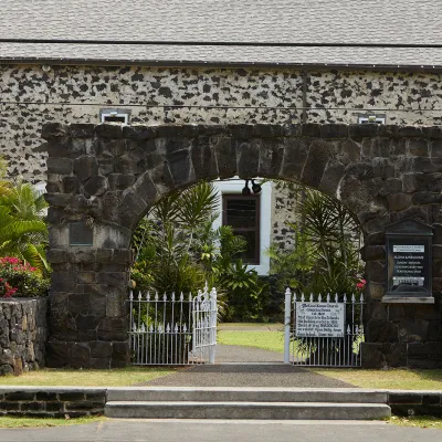 Stone building and white gate in Historic Kailua Village, surrounded by tropical greenery.