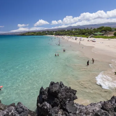Wide view of Hapuna Beach with turquoise waters, white sand, and visitors enjoying the shoreline on a sunny day.