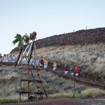 Visitors walking toward Puukohola Heiau, a historic temple surrounded by dry grassland under a clear blue sky.