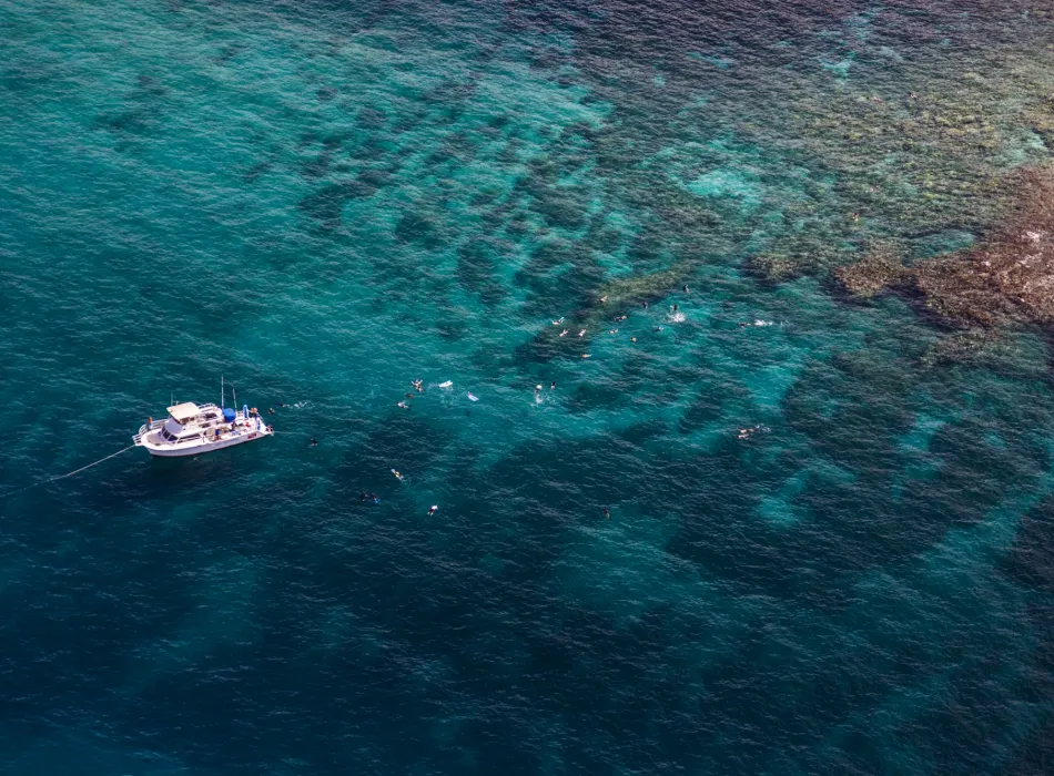 Aerial view of a boat anchored near a vibrant coral reef, with snorkelers exploring the clear turquoise water of Maui..