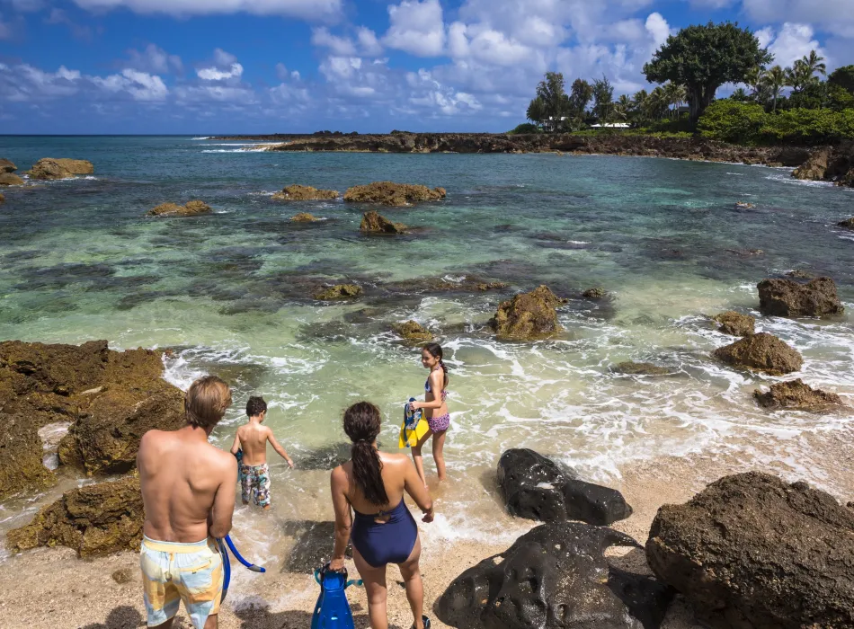 Family wading into a clear turquoise tide pool to snorkel.
