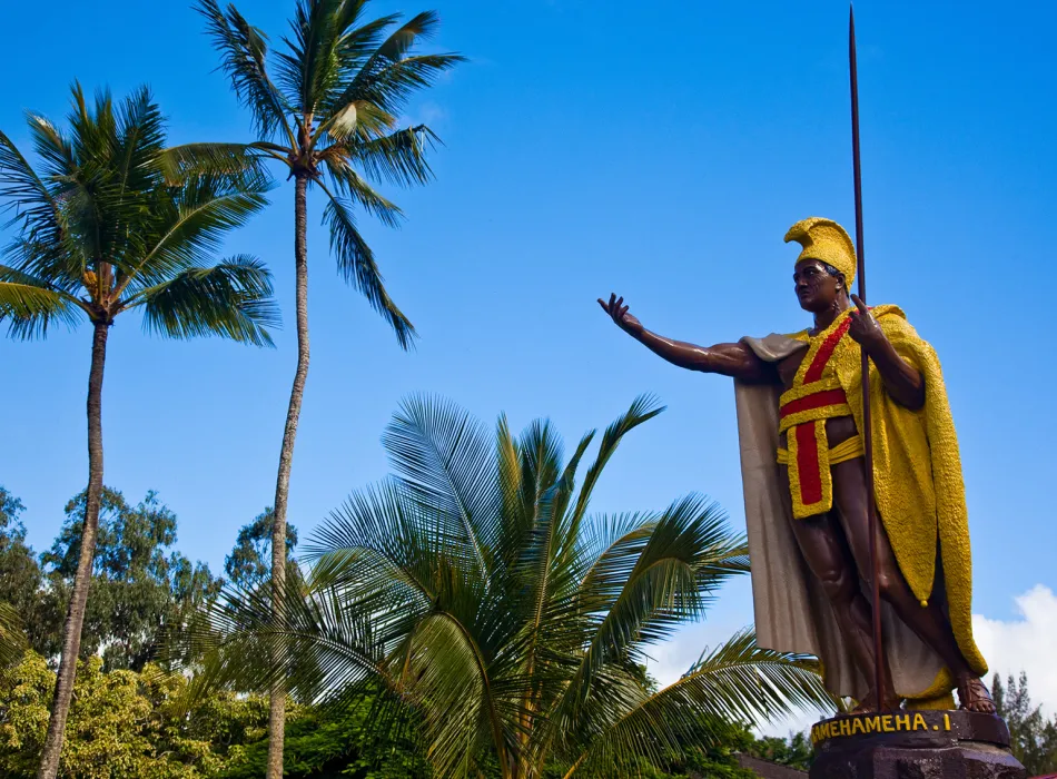 Statue of King Kamehameha I in Kapaau, adorned with a golden cape and surrounded by palm trees under a bright blue sky