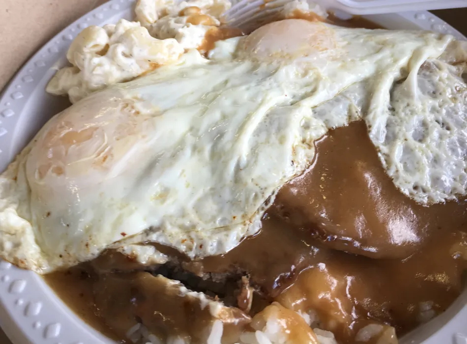 Plate of Hawaiian loco moco featuring rice topped with a hamburger patty, fried egg, and rich brown gravy.